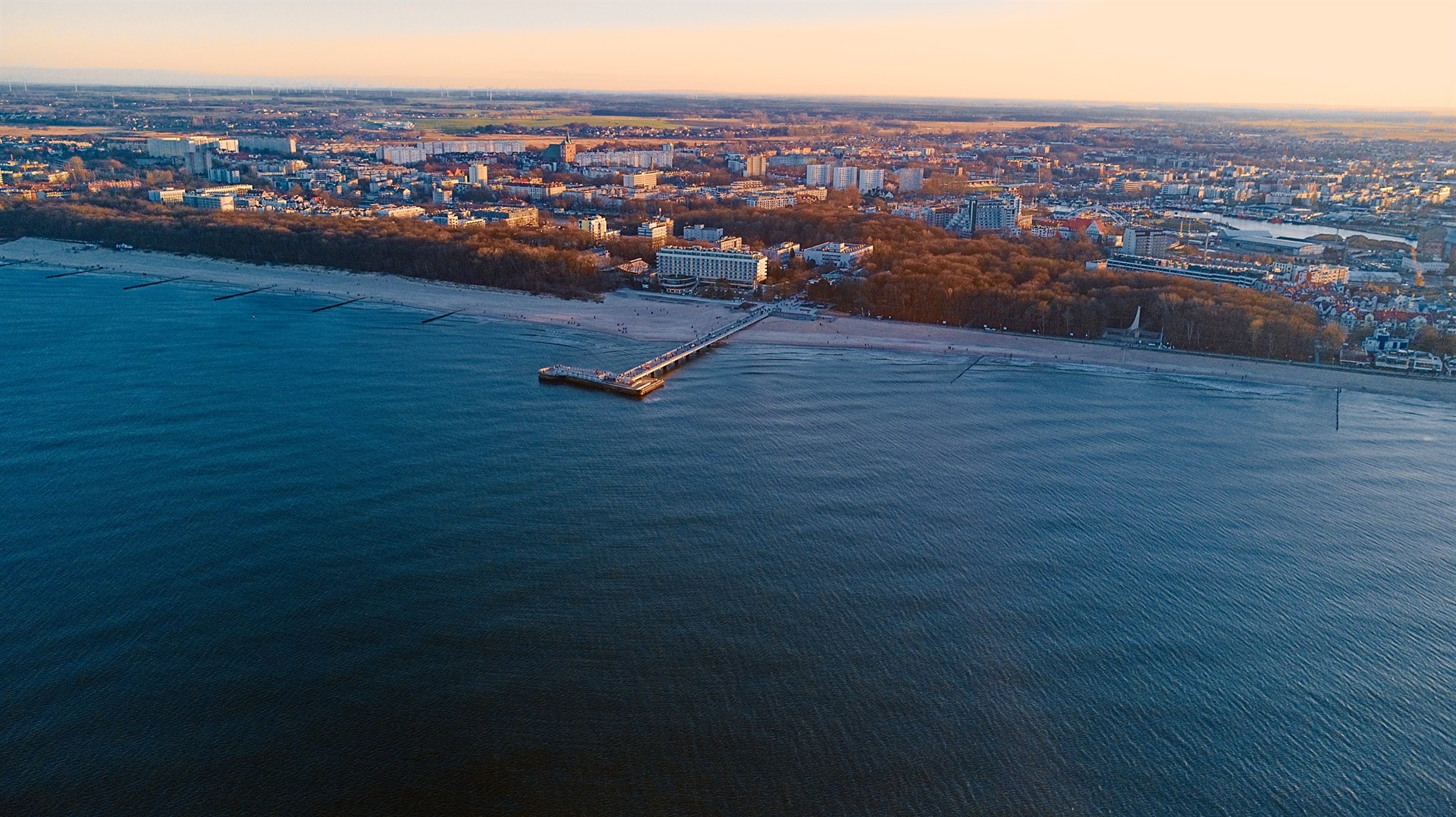 Nadmorska panorama z piaszczystą plażą, długim molo wchodzącym w spokojne niebieskie morze