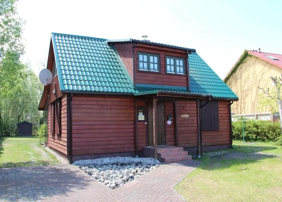 Drewniany czerwono-brązowy dom z zielonym dachem, lukarną, małym gankiem i anteną satelitarną
