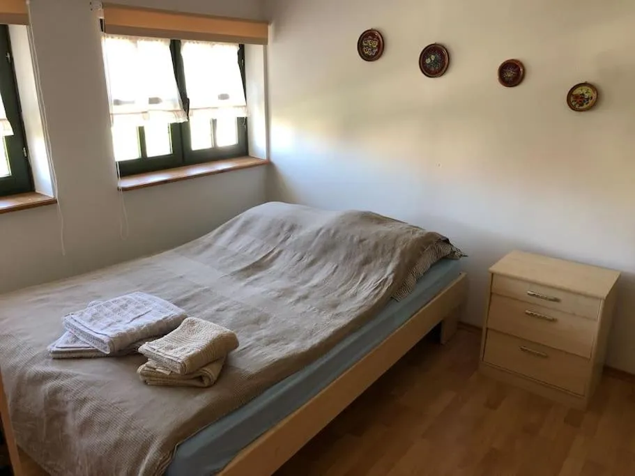 Sypialnia z podwójnym łóżkiem w beżowej pościeli, złożonymi ręcznikami, drewnianą szafką nocną i oknem